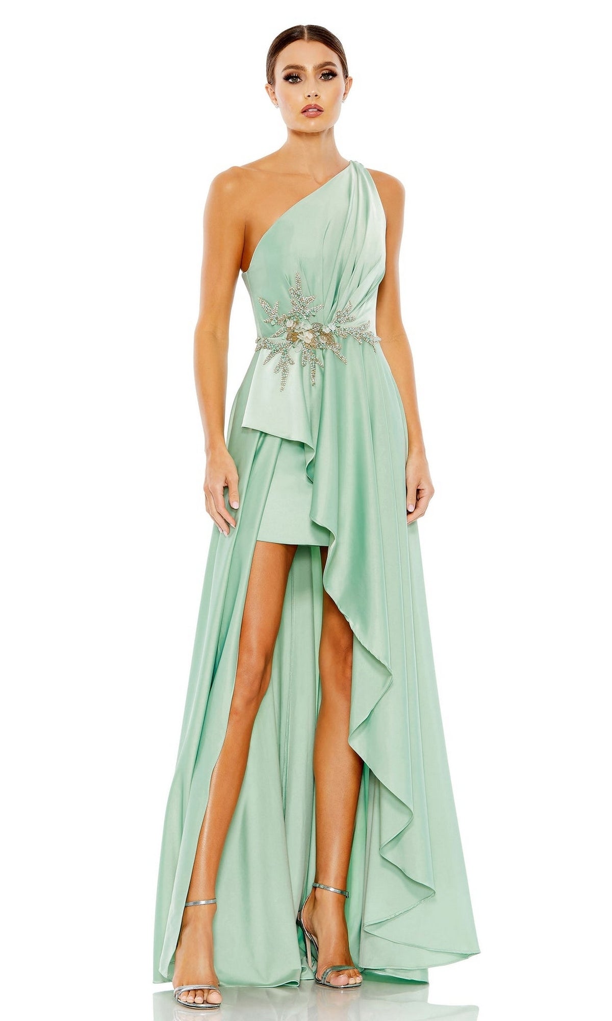 A woman wears the Long Formal Dress 11262 by Mac Duggal, a mint green pastel one-shoulder gown with an embellished waist, paired with silver high-heeled sandals.